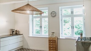 Eine geräumige Küche mit einem großen Fenster, einer Pendelleuchte und einer Wanduhr.