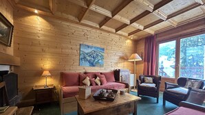 Interior acogedor de una cabaña de troncos con techo de madera, un sofá, una silla, una mesita de café y un cuadro en la pared.