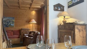 Un interior de madera con una mesa de comedor para cuatro personas, una lámpara y un cuadro en la pared.