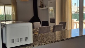 Una cocina moderna con estufa integrada, un comedor con mesa y sillas, y vistas al exterior a través de una puerta corrediza.