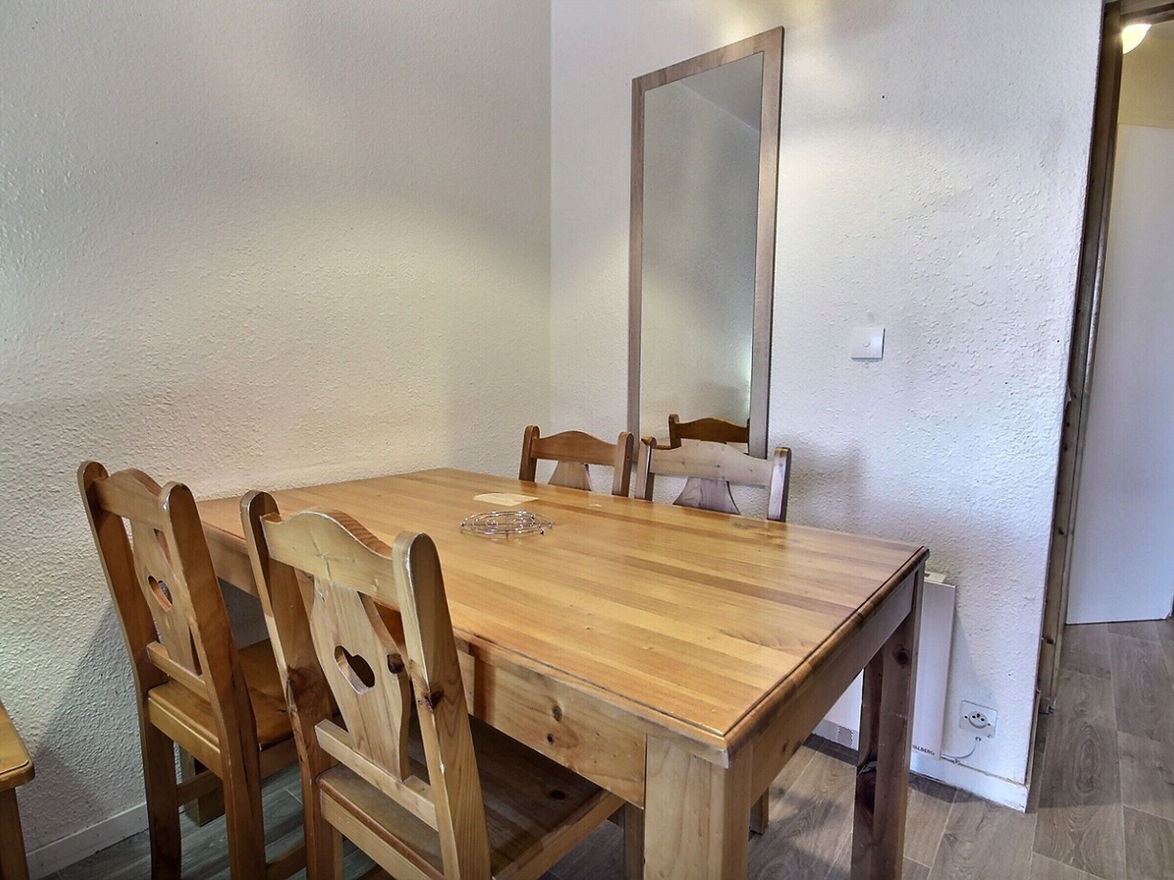 Una mesa de madera para comer con cuatro sillas, un espejo en la pared y un enchufe en la pared.