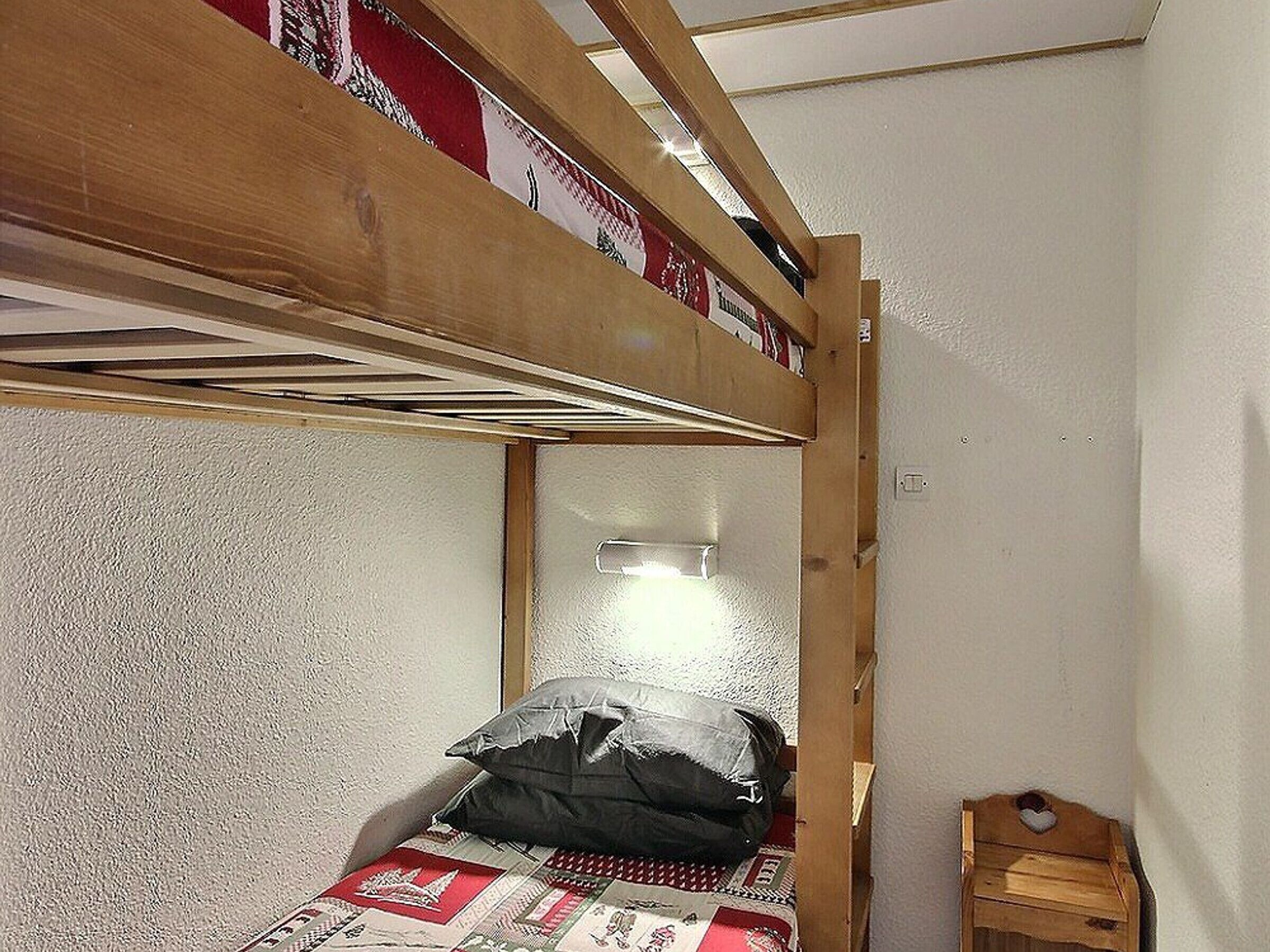 A bunk bed with a wooden headboard, a small bedside table, and a red and white patterned bedspread.