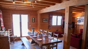 A wooden interior with a long dining table set for four, chairs, a bench, and a red sofa. - Spacious chalet for 10 near slopes with private parking (Le Grand-Bornand)