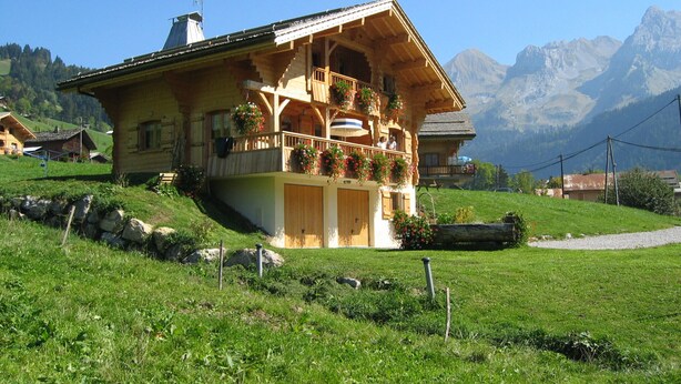 A chalet with a balcony, surrounded by a lush green landscape and mountains in the background. - Spacious chalet for 10 near slopes with private parking (Le Grand-Bornand)