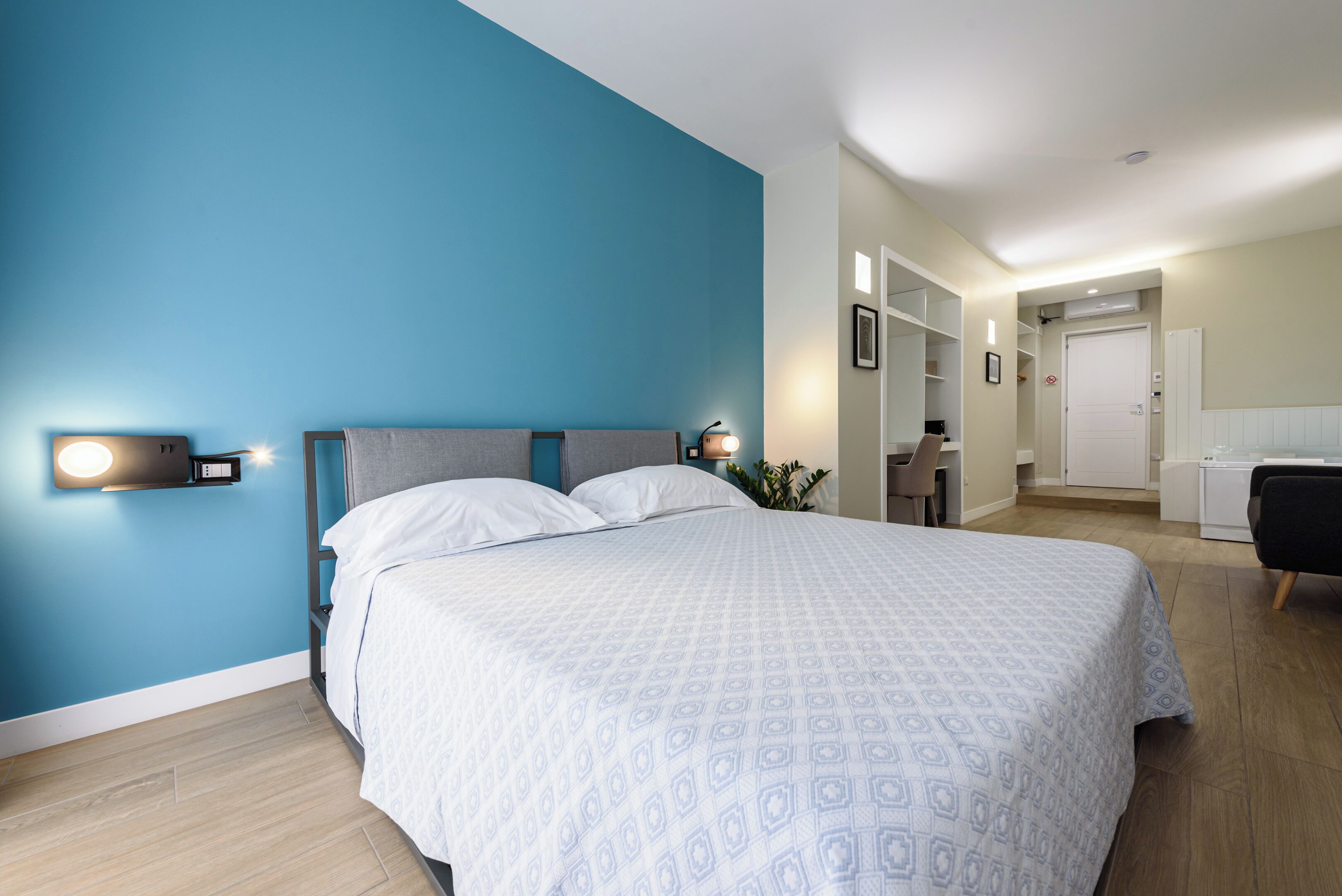 A modern bedroom with a large bed, a nightstand, a wall-mounted lamp, and a desk area with a chair.