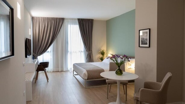 Una habitación de hotel moderna con cama, una mesa redonda para comer, una silla, televisor y ventana con cortinas.
