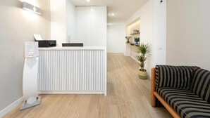 Un área de recepción con un mostrador blanco, un escritorio, una planta en maceta y un sofá a rayas.
