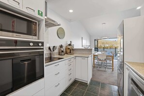 A modern kitchen with a microwave, oven, and dishwasher, a dining area with a table and chairs, and a large window offering a view.