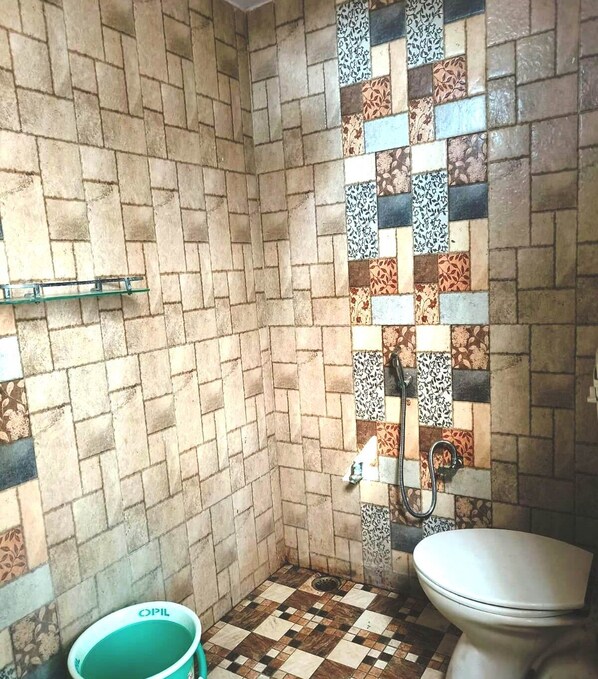 Een badkamer met een betegelde douche, een toilet en een groene emmer.