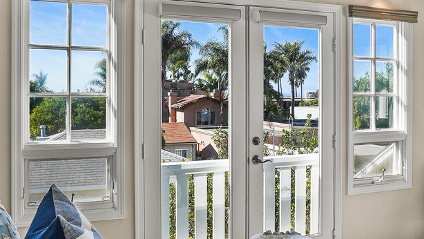 A bedroom with a large bed, two windows, and a view of palm trees and houses. - Lovely home with backyard oasis & great WiFi - walk to La Jolla Village, dogs OK (La Jolla)