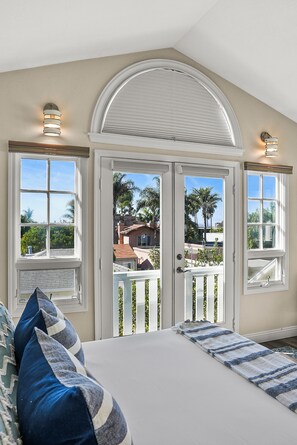 Un dormitorio con una cama grande, dos ventanas y vistas a palmeras y casas.