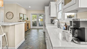 A modern kitchen with a large island, white cabinetry, a coffee maker, and a clock on the wall. - Lovely home with backyard oasis & great WiFi - walk to La Jolla Village, dogs OK (La Jolla)