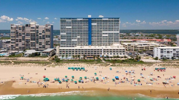 A coastal hotel with multiple buildings, a sandy beach, and umbrellas. - Direct Oceanfront Condo with the Best Amenities (Ocean City)