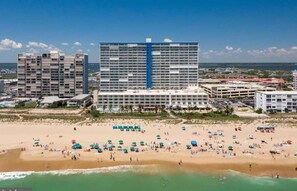 Un hôtel situé sur la côte, composé de plusieurs bâtiments, avec une plage de sable et des parasols.