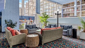 A spacious indoor area with wicker furniture, a patterned carpet, and a view of a building with balconies. - Direct Oceanfront Condo with the Best Amenities (Ocean City)
