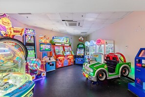 Um salão de jogos com diversos aparelhos, incluindo um carrinho de brinquedo verde e uma roleta grande giratória.