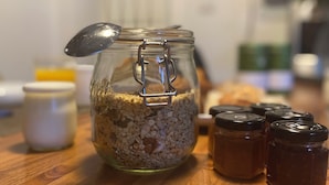 A glass jar with a metal clasp lid filled with oats, surrounded by other jars and a spoon on a wooden surface. - Maison Auguste (Paris)
