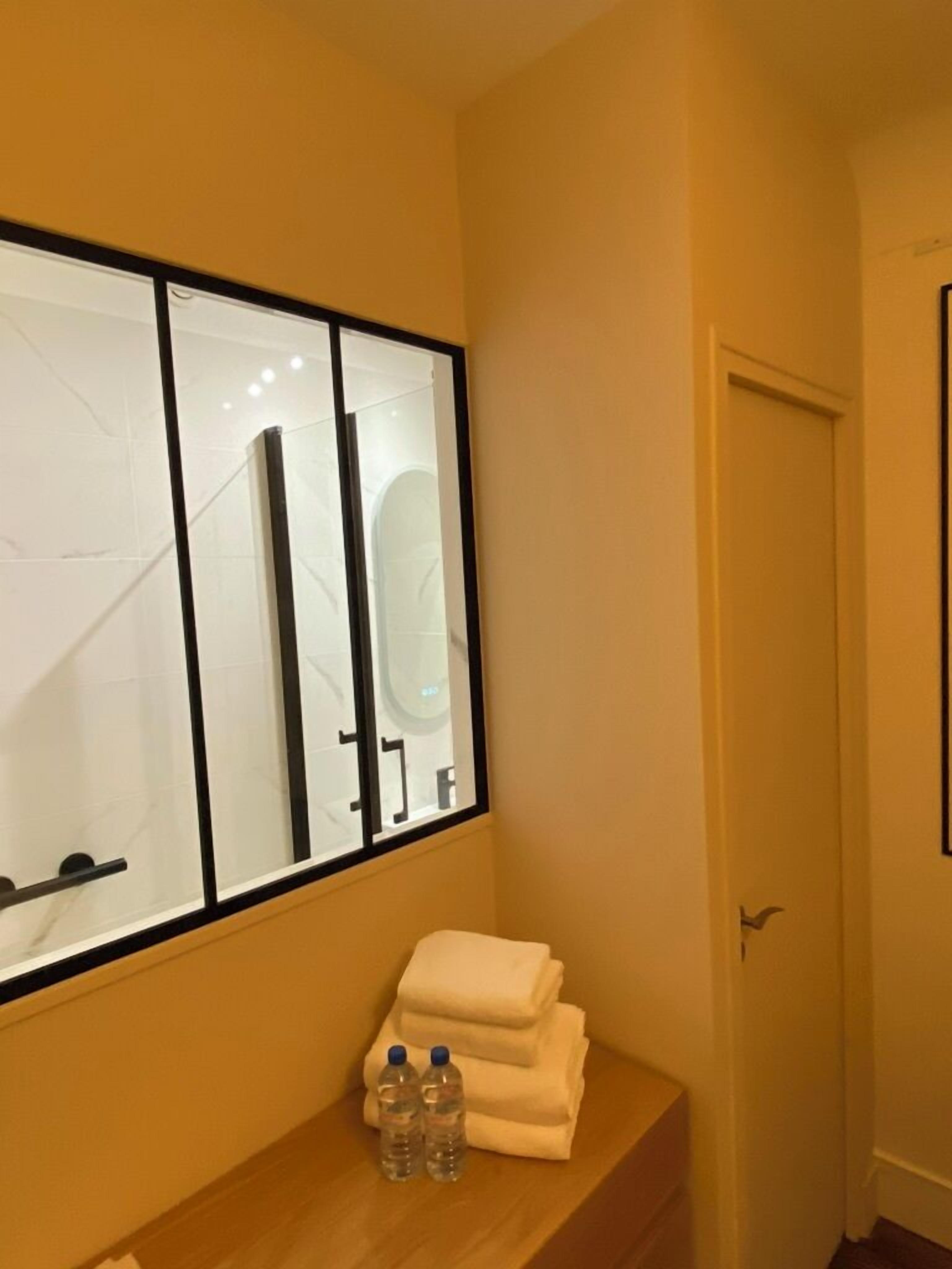 Une salle de bain avec un miroir, un porte-serviettes et deux bouteilles d’eau posées sur un comptoir en bois.