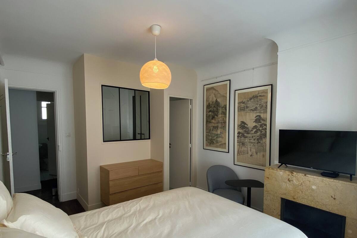 A hotel room with a large bed, a wooden dresser, a desk with a chair, a television, and two framed pictures on the wall.