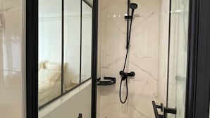 A modern shower with a glass door, a handheld showerhead, and a handheld shower attachment. - Maison Auguste (Paris)