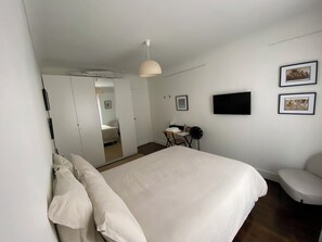 A bedroom with a large bed, a desk, a chair, a TV, and two framed pictures on the wall. - Maison Auguste (Paris)