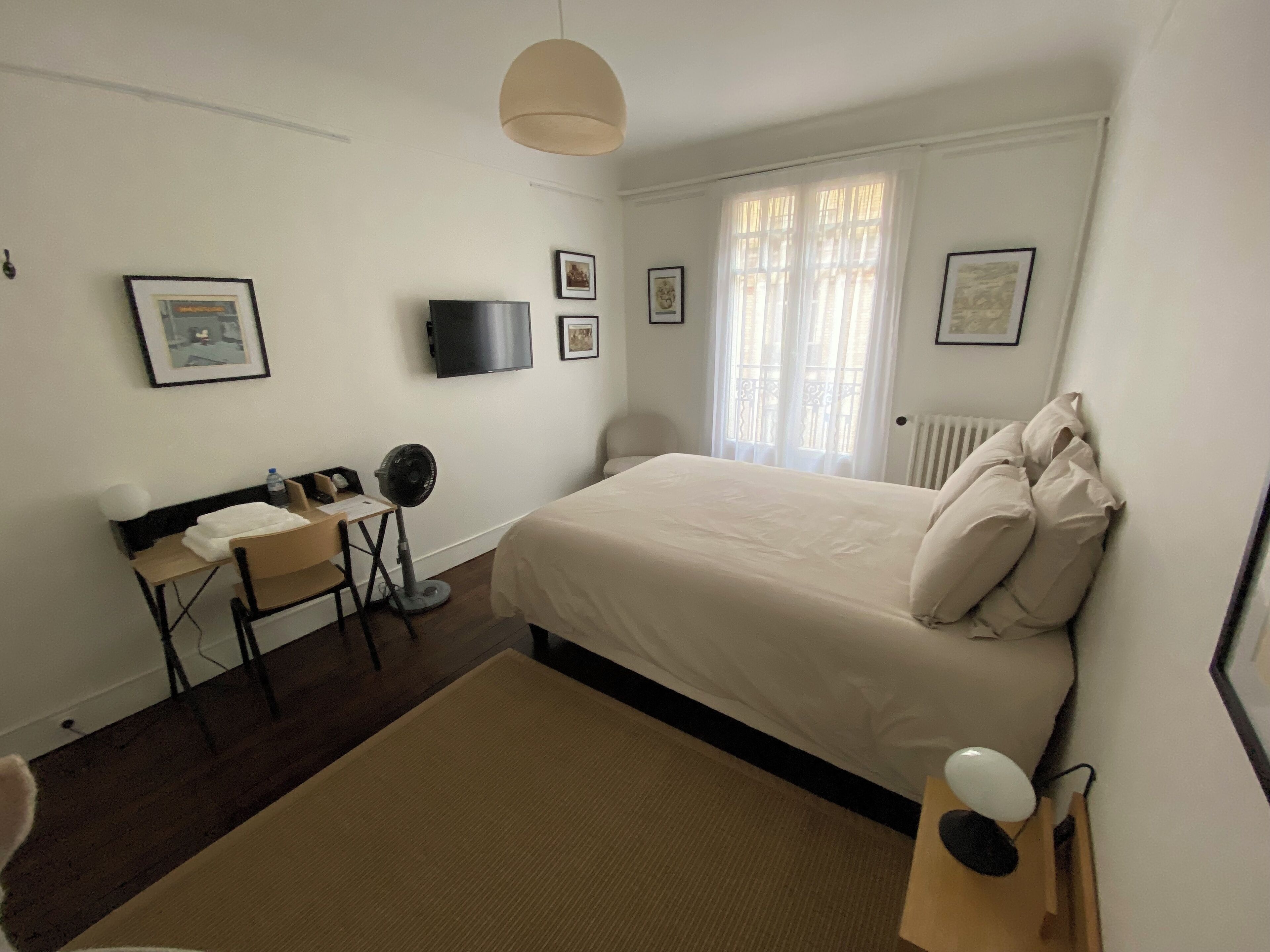 Une chambre à coucher avec un lit, un bureau, une chaise, une télévision et des tableaux encadrés accrochés au mur.