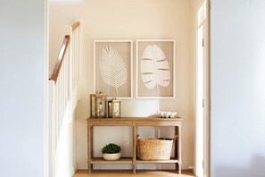 A hallway with a wooden staircase, a console table with decorative items, and two framed leaf artworks.