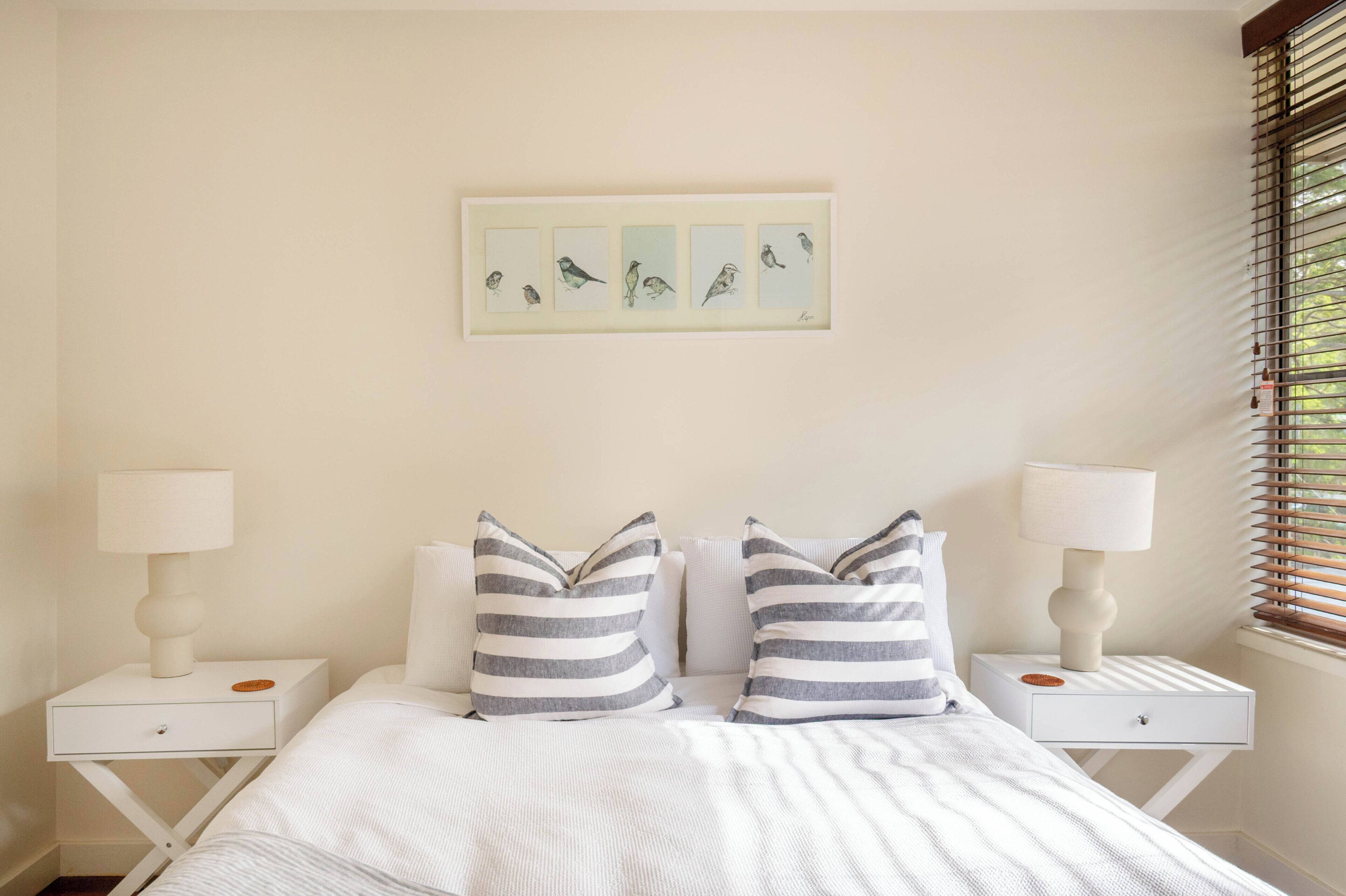 Un dormitorio con una cama, dos mesitas de noche con lámparas y una obra de arte enmarcada en la pared.