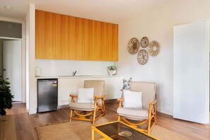 A modern kitchen with wooden cabinets, a built-in dishwasher, and a dining area with two wicker chairs and a glass coffee table.
