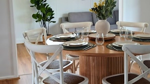 A dining area with a round wooden table set for six, surrounded by white chairs. - Capel Sound Hideaway (Capel Sound)