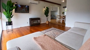 A living room with a sofa, a TV, a fireplace, and a dining area in the background. - Capel Sound Hideaway (Capel Sound)