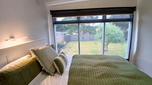 A bedroom with a large window, a bed with green bedding, and a view of a backyard. - Capel Sound Hideaway (Capel Sound)