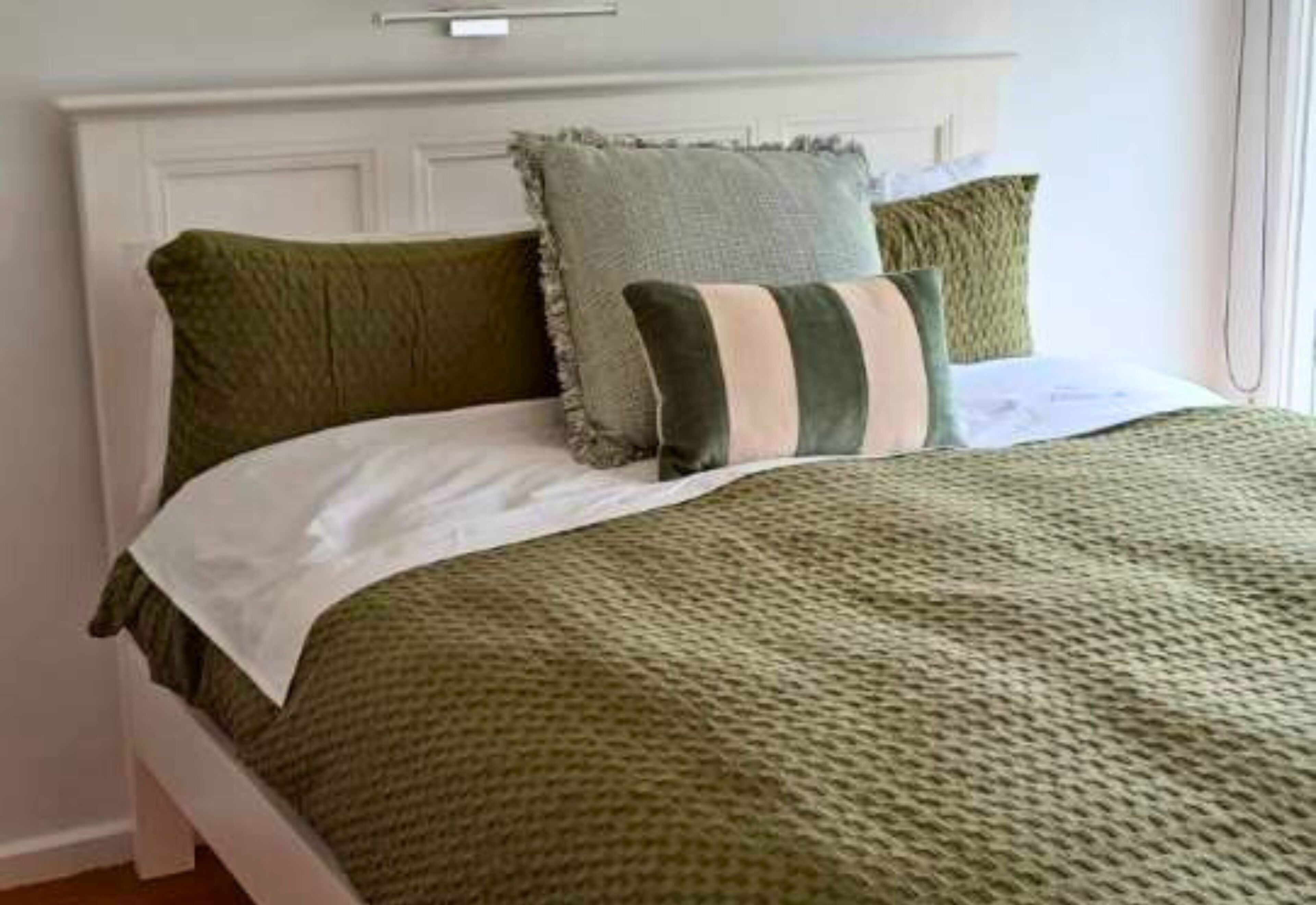 Una cama con cabecera blanca, ropa de cama verde y almohadas a rayas.