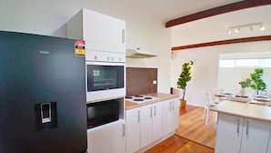 A modern kitchen with a black refrigerator, white cabinets, a stove, and a microwave. There is a dining area with a table and chairs, and a potted plant. - Capel Sound Hideaway (Capel Sound)