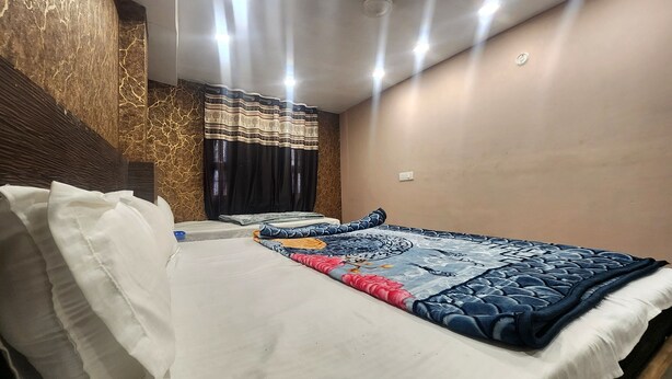A hotel room with a bed, a headboard, a wall with a textured pattern, a window with curtains, and a ceiling with recessed lighting. - Hotel Swagat Palace (New Delhi)
