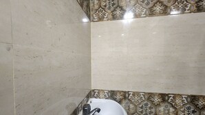 A corner bathroom with a white sink, decorative patterned tiles, and a plain tiled wall. - Hotel Swagat Palace (New Delhi)