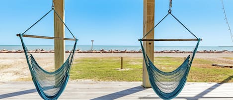A wooden deck with two hanging hammocks overlooking a beach.