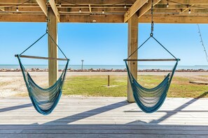 Una terraza de madera con dos hamacas colgantes que dan a una playa.