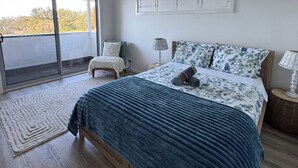 Een slaapkamer met een groot bed, een stoel, een nachtkastje en uitzicht door een schuifdeur.