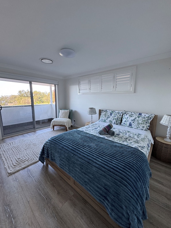 A bedroom with a large bed, a chair, a bedside table, and a view through a sliding door. - Sydney Waterfront Beach House (Taren Point)
