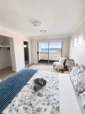 A bedroom with a bed, a chair, a lamp, and a view of the sea through a sliding door.