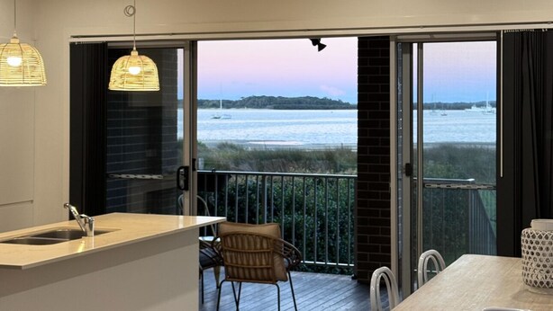 Een moderne keuken met een groot raam en schuifdeuren die leiden naar een balkon met uitzicht op een wateroppervlak.