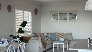 Een moderne woonkamer met een grijze bank, witte stoelen, een klein wit tafeltje en een keuken met een wit aanrechtblad en een spoelbak.
