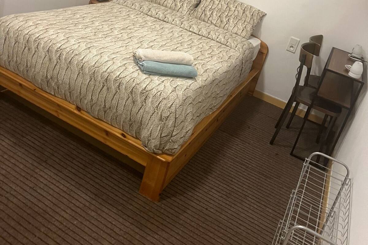 Une chambre à coucher avec un lit en bois, une petite table, une chaise et un radiateur.