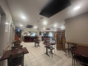 A restaurant with multiple tables and chairs, a counter with a menu, and a television mounted on the wall. - Le Manteau Bleu (Béziers)