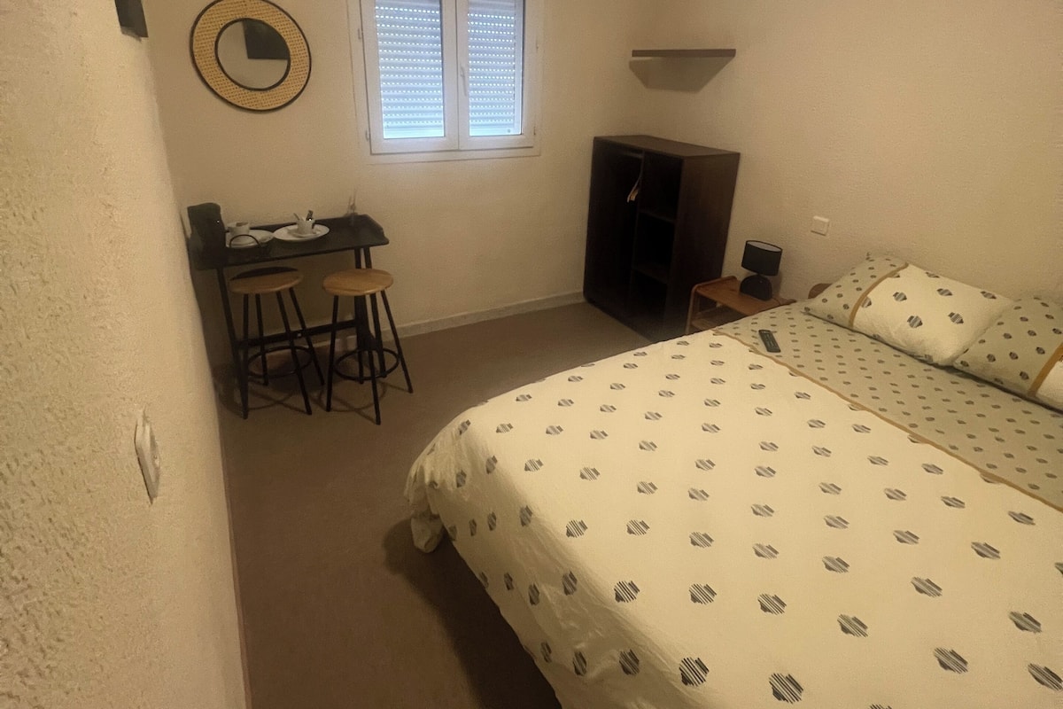 Une chambre à coucher comprenant un lit, un bureau, une chaise, un téléviseur et une fenêtre avec des stores.