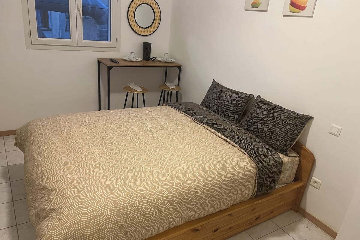 Une chambre avec un lit en bois, une couvre-lit à motifs et des coussins assortis. On y trouve une petite table de chevet avec deux tasses et une télécommande.