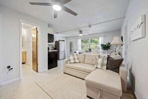 A modern living room with a sofa, a coffee table, and a lamp. There is a kitchen area with a refrigerator and cabinets.