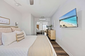 Une chambre à coucher avec un lit, une table de chevet, une commode, un téléviseur et un tableau encadré au mur.