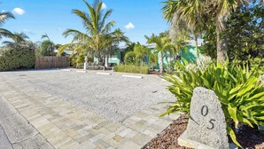 Alameda pavimentada que leva a um edifício com uma placa de número '05', em um jardim com palmeiras e arbustos.